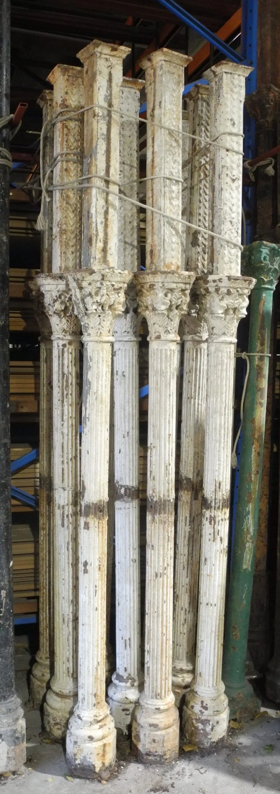 A tall stack of several salvaged, distressed white cast iron columns with fluted shafts and decorative capital and base sections, likely for a verandah or portico restoration project.