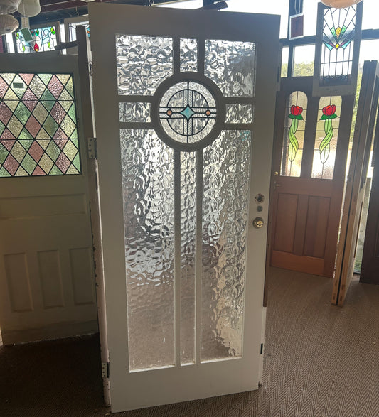 An original salvaged Federation style timber door painted white, featuring an upper window panel with textured privacy glass and a red and green leadlight floral design on display at Chippendale Restorations.