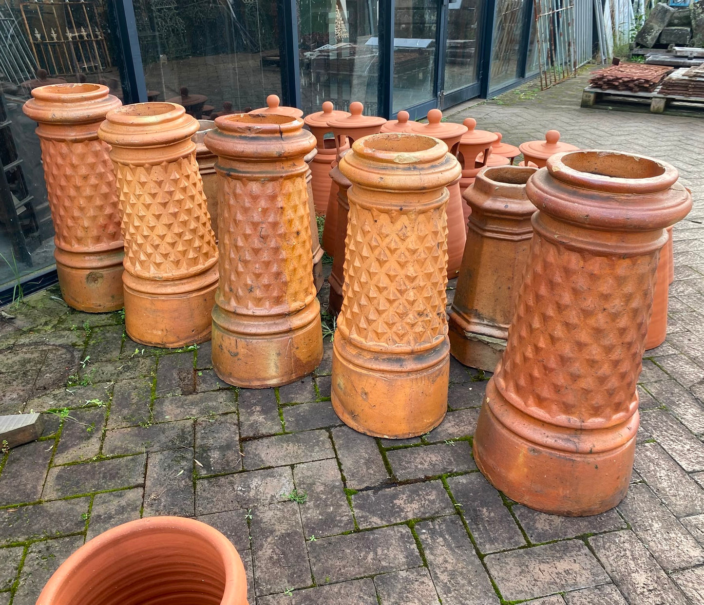 A matching set of five authentic salvaged Victorian terracotta chimney pots featuring a distinctive embossed diamond-lattice texture, lined up on pavers at the Chippendale Restorations heritage building yard.