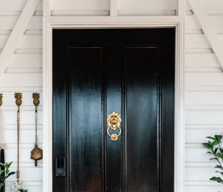 Traditional regency style lion head door knocker in polished brass and matte black finishes, shown mounted on a classic paneled front door.