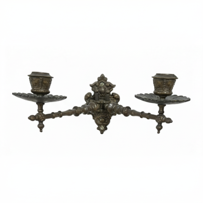 Vintage ornate cast metal wall sconce featuring a central decorative mount and two symmetrical arms, each holding a candle cup and drip tray, ready for wall mounting.