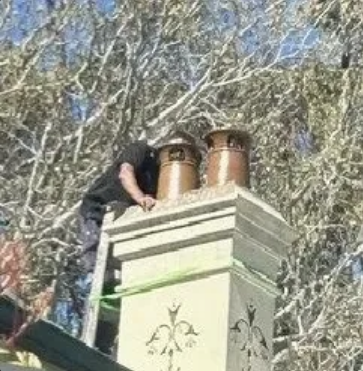 Person climbing a chimney with copper stacks against a tree-lined background
