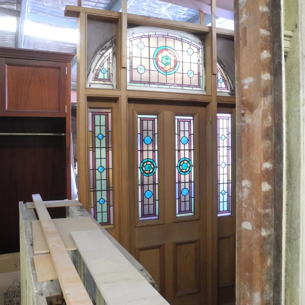 Grand pair of turn of the century solid timber entranceway doors featuring arched leadlight window panes with crimson and amber stained glass accents from Chippendale Restorations second hand doors.