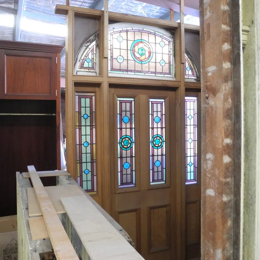 Grand pair of turn of the century solid timber entranceway doors featuring arched leadlight window panes with crimson and amber stained glass accents from Chippendale Restorations second hand doors.
