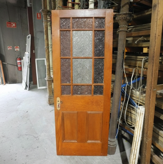 An original salvaged timber Federation gallery door painted white, showcasing an upper window with multi-lite red and amber glass framing a rare central pane of pressed flannel flower privacy glass at Chippendale Restorations.
