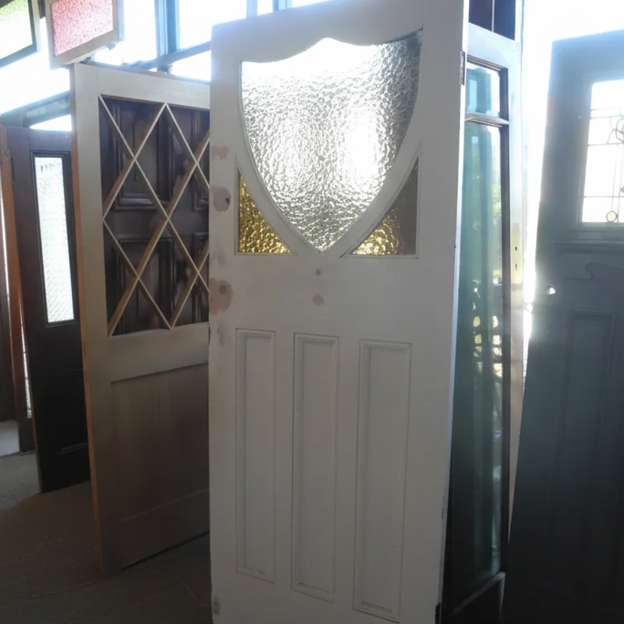 Authentic 1920s Edwardian solid timber front door featuring a distinctive shield-shaped privacy glass window with amber corner accents, available to buy at Chippendale Restorations second hand doors yard.
