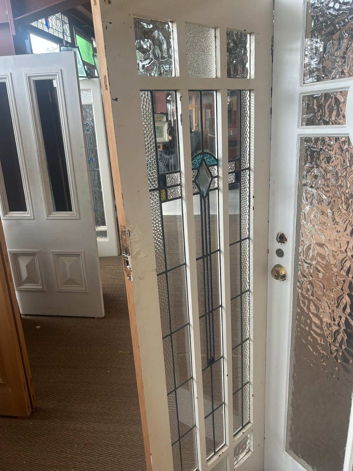An original salvaged timber Federation entry door painted white, showcasing an elongated vertical window with multi-lite privacy leadlight glass and a central turquoise accents layout inside the Chippendale Restorations architectural salvage showroom.