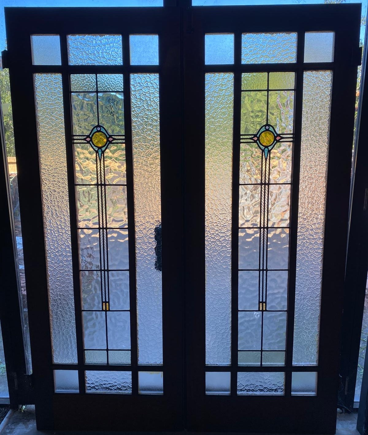 A pair of original salvaged 1920s timber French doors with three vertically stacked textured privacy glass window panels featuring subtle green and amber leadlight geometric motifs, shown in the Chippendale Restorations salvage workshop.