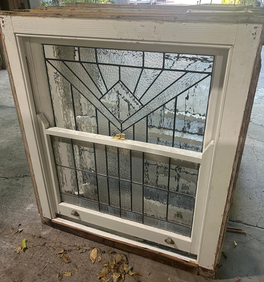 An original salvaged single hung timber window in a dark frame, featuring a top sash with textured privacy glass and green and amber leadlight detailing on display at Chippendale Restorations.