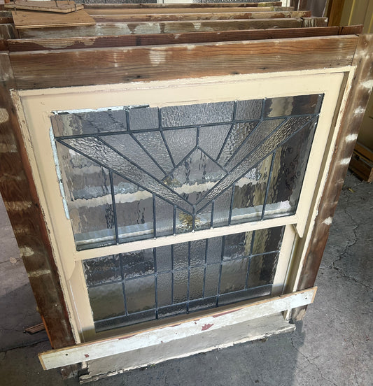 An original salvaged single hung timber window in a dark frame, featuring a top sash with textured privacy glass and green and amber leadlight detailing on display at Chippendale Restorations.