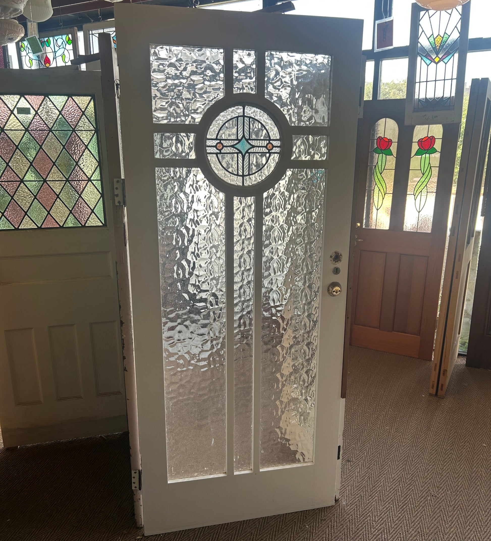 An original salvaged Federation style timber door painted white, featuring an upper window panel with textured privacy glass and a red and green leadlight floral design on display at Chippendale Restorations.