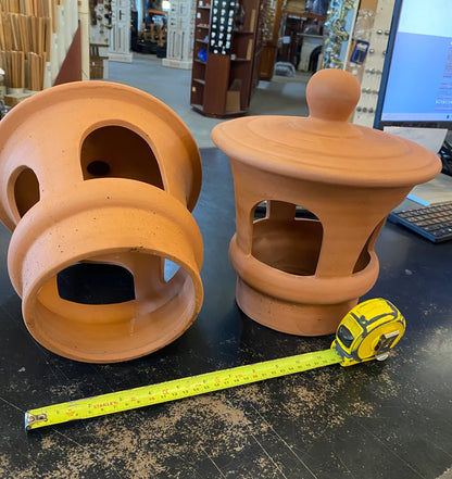 Traditional terracotta chimney cowl with open arched side vents and a ball finial top cover, sitting on a counter at Chippendale Restorations showroom.