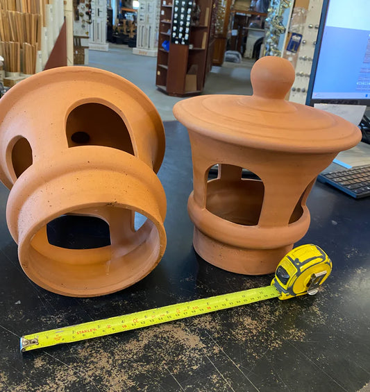 Traditional terracotta chimney cowl with open arched side vents and a ball finial top cover, sitting on a counter at Chippendale Restorations showroom.