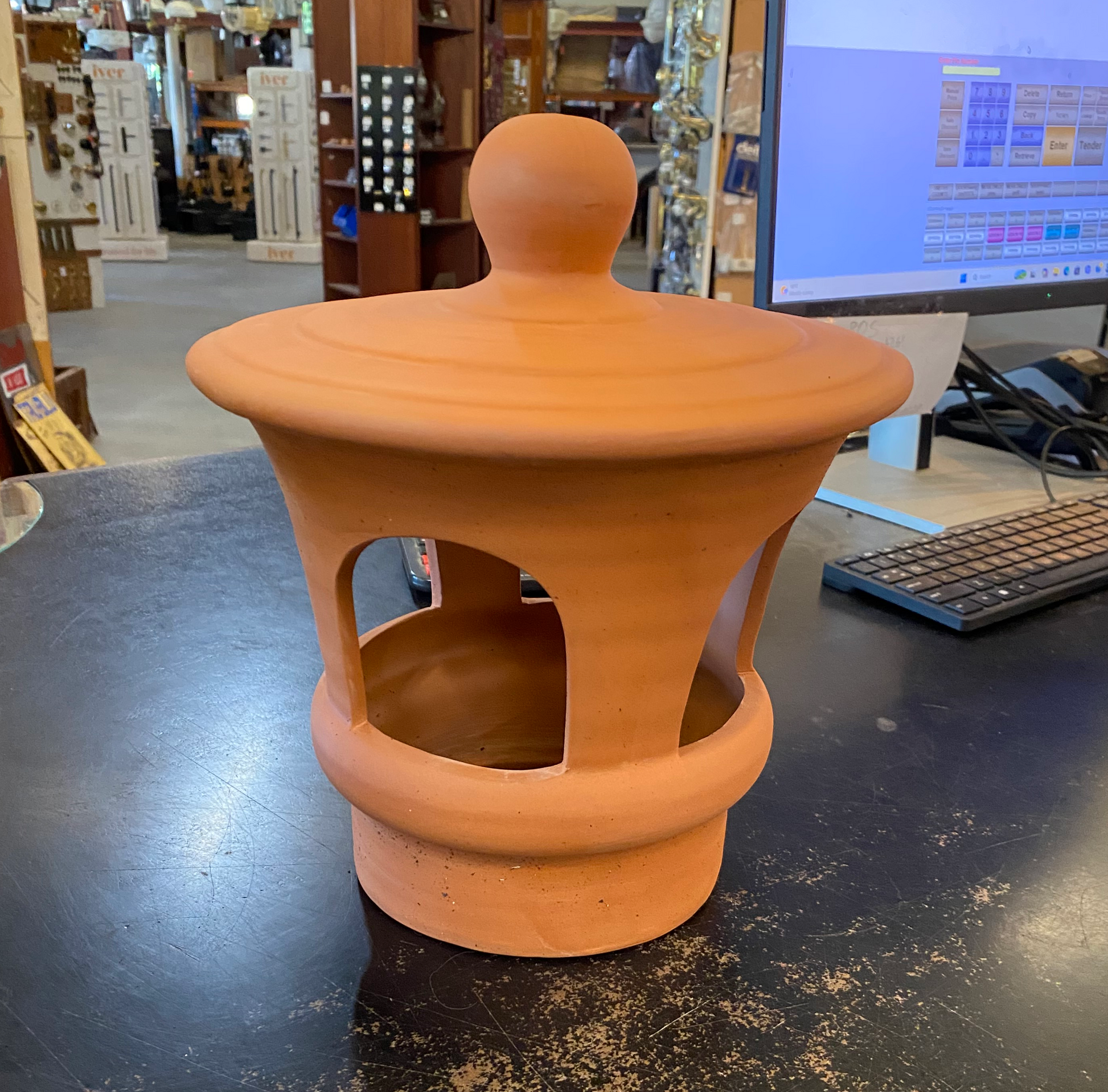 Traditional terracotta chimney cowl with open arched side vents and a ball finial top cover, sitting on a counter at Chippendale Restorations showroom.