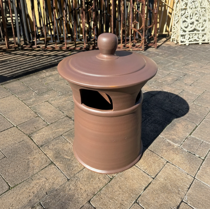 An original large dark glazed terracotta chimney pot with a weathered finish and horizontal ribbing, displayed outside at the Chippendale Restorations architectural salvage yard.