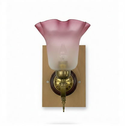 Vintage brass wall sconce with a decorative arm, a polished wood roundel and square backplate, and a red and frosted clear fluted glass lampshade.