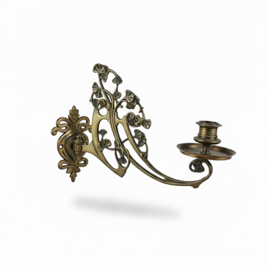 Highly ornate Art Nouveau-style single candle sconce made of brass, featuring an elaborate backplate and a curved arm with decorative leaf motifs, ending in a candle cup and drip tray.