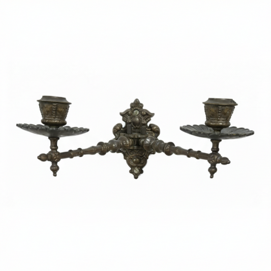 Vintage ornate cast metal wall sconce featuring a central decorative mount and two symmetrical arms, each holding a candle cup and drip tray, ready for wall mounting.