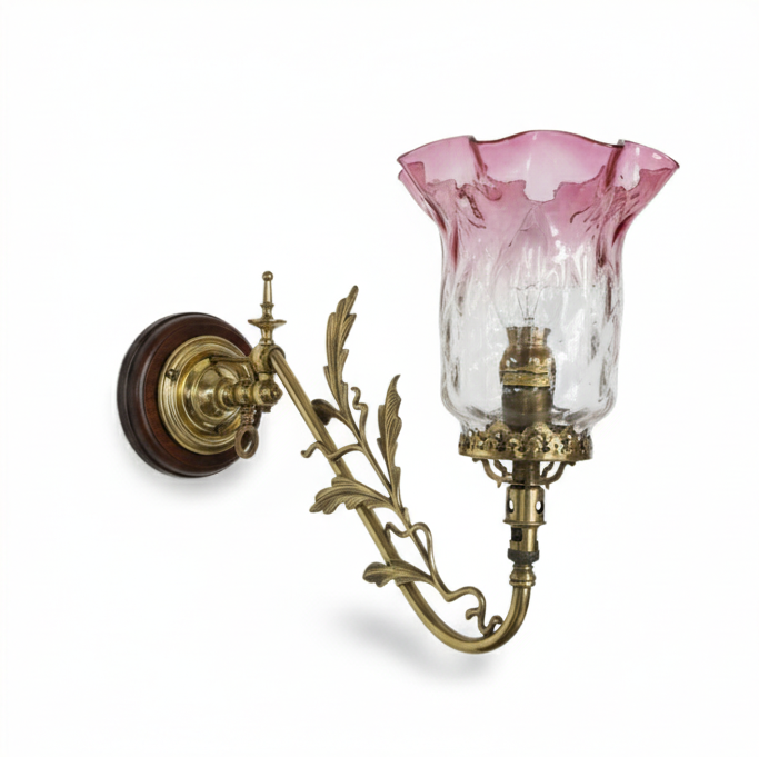 Vintage ornate brass wall sconce featuring a curved arm, a decorative wood and brass wall plate, and a pink and clear textured fluted glass shade.