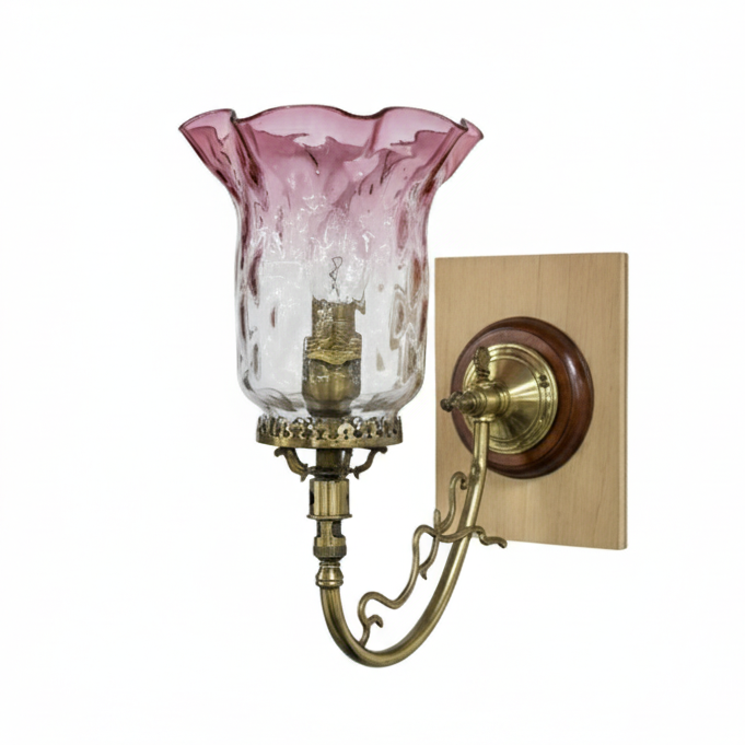 Vintage ornate brass wall sconce featuring a curved arm, a decorative wood and brass wall plate, and a pink and clear textured fluted glass shade.