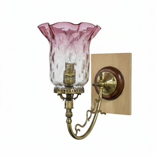 Vintage ornate brass wall sconce featuring a curved arm, a decorative wood and brass wall plate, and a pink and clear textured fluted glass shade.