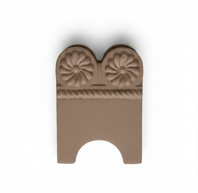 A single, curved, unglazed terracotta garden edge tile featuring an embossed design of two central daisy flowers above a twisted rope pattern, isolated on a white background.