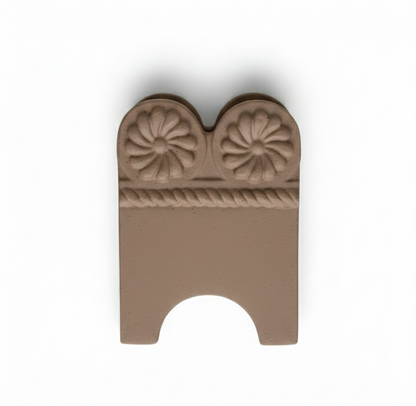 A single, curved, unglazed terracotta garden edge tile featuring an embossed design of two central daisy flowers above a twisted rope pattern, isolated on a white background.