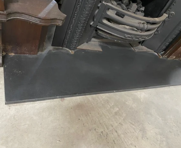Honed black granite hearth slab featuring a smooth matte non-reflective finish fitted under a vintage cast iron fireplace