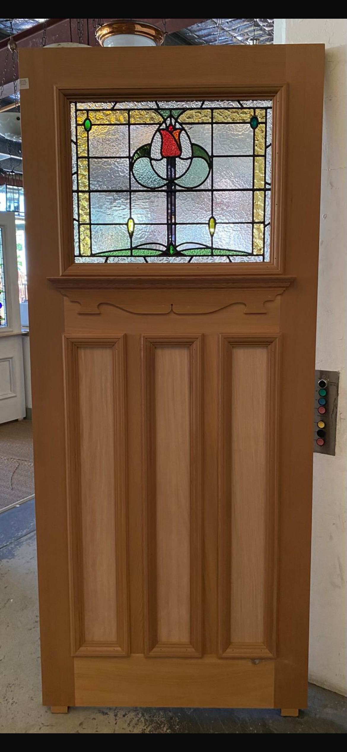 New Edwardian style front door made of Western Red Cedar, featuring a single, wide leadlight glass panel above three vertical timber panels. The leadlight design depicts a central stylized red tulip or rose on a stem, with green and yellow accents and a clear textured background.