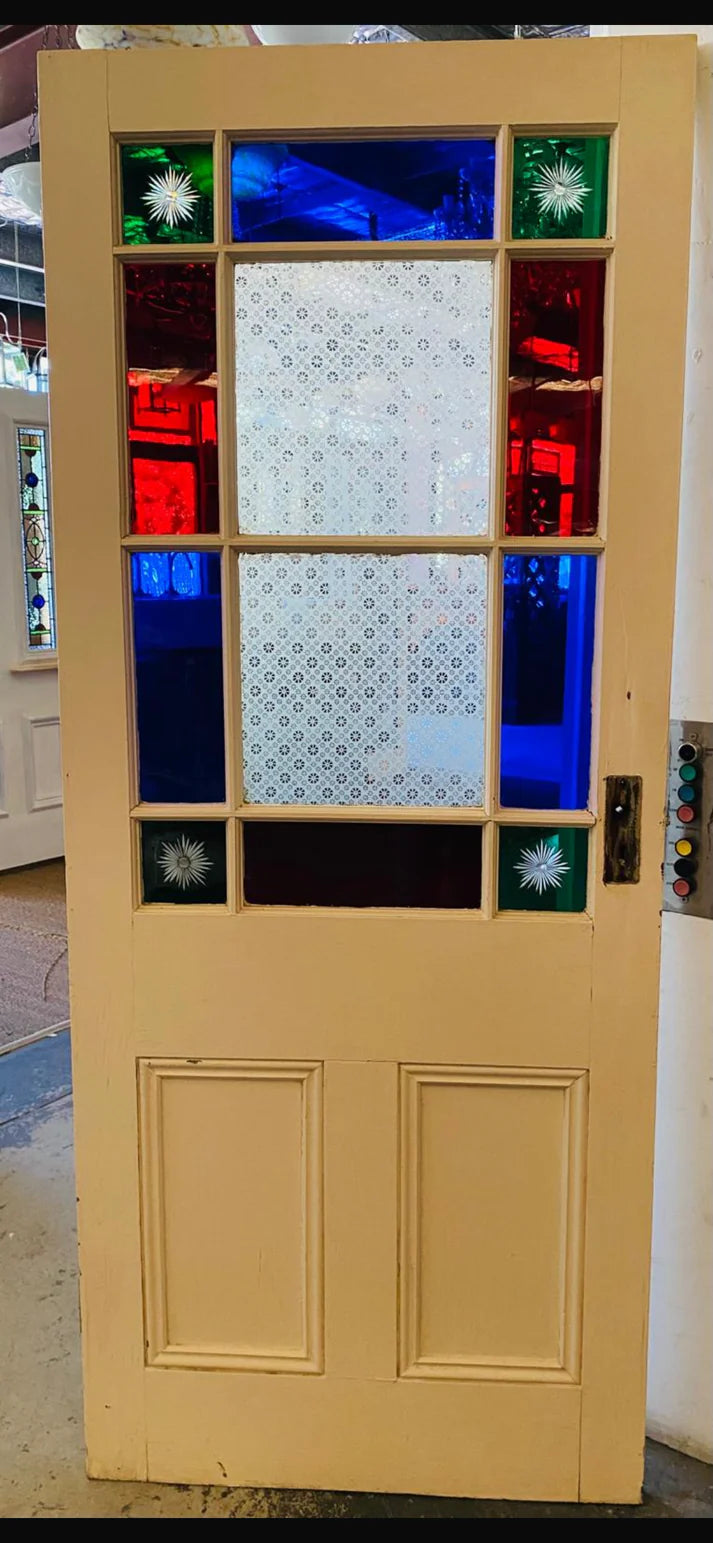 An original salvaged Victorian timber gallery door featuring multi-lite red, blue, and patterned privacy glass windows with four green starburst brilliant-cut corners on display at Chippendale Restorations.