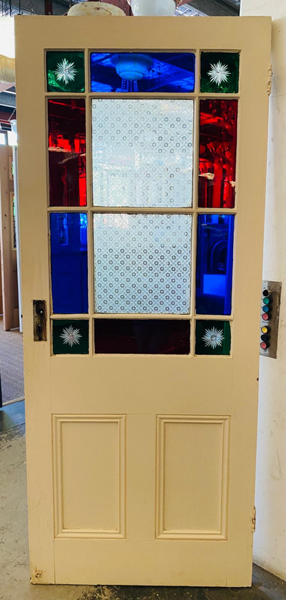 Original Victorian internal door with multiple coloured stained glass panels. The door is cream-coloured with two raised lower panels. The glass features a large central clear patterned section surrounded by vibrant red and blue glass, with small green corner panels containing brilliant cut starburst designs.