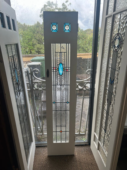An original salvaged narrow Federation style timber door painted white, showcasing an upper window panel with beautiful red, amber, and green geometric leadlight privacy glass on display at Chippendale Restorations.