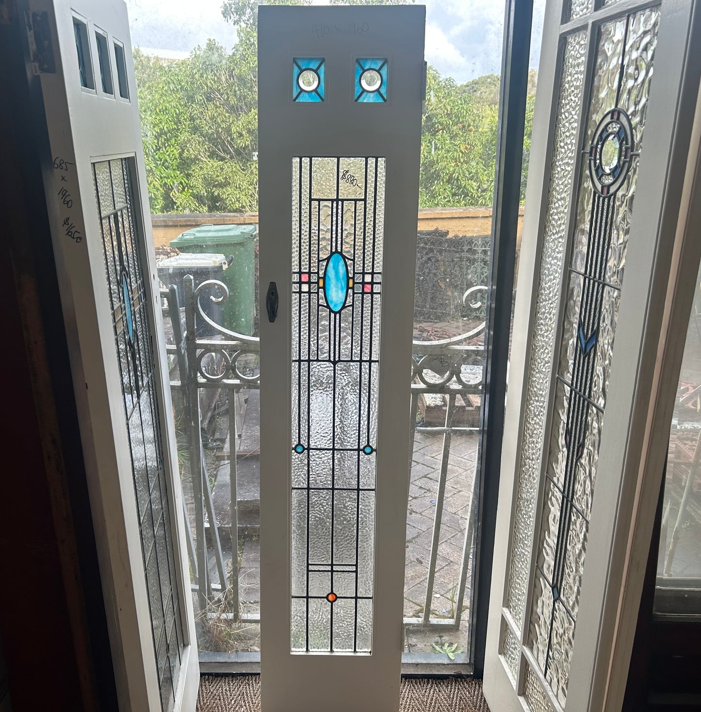 An original salvaged narrow Federation style timber door painted white, showcasing an upper window panel with beautiful red, amber, and green geometric leadlight privacy glass on display at Chippendale Restorations.