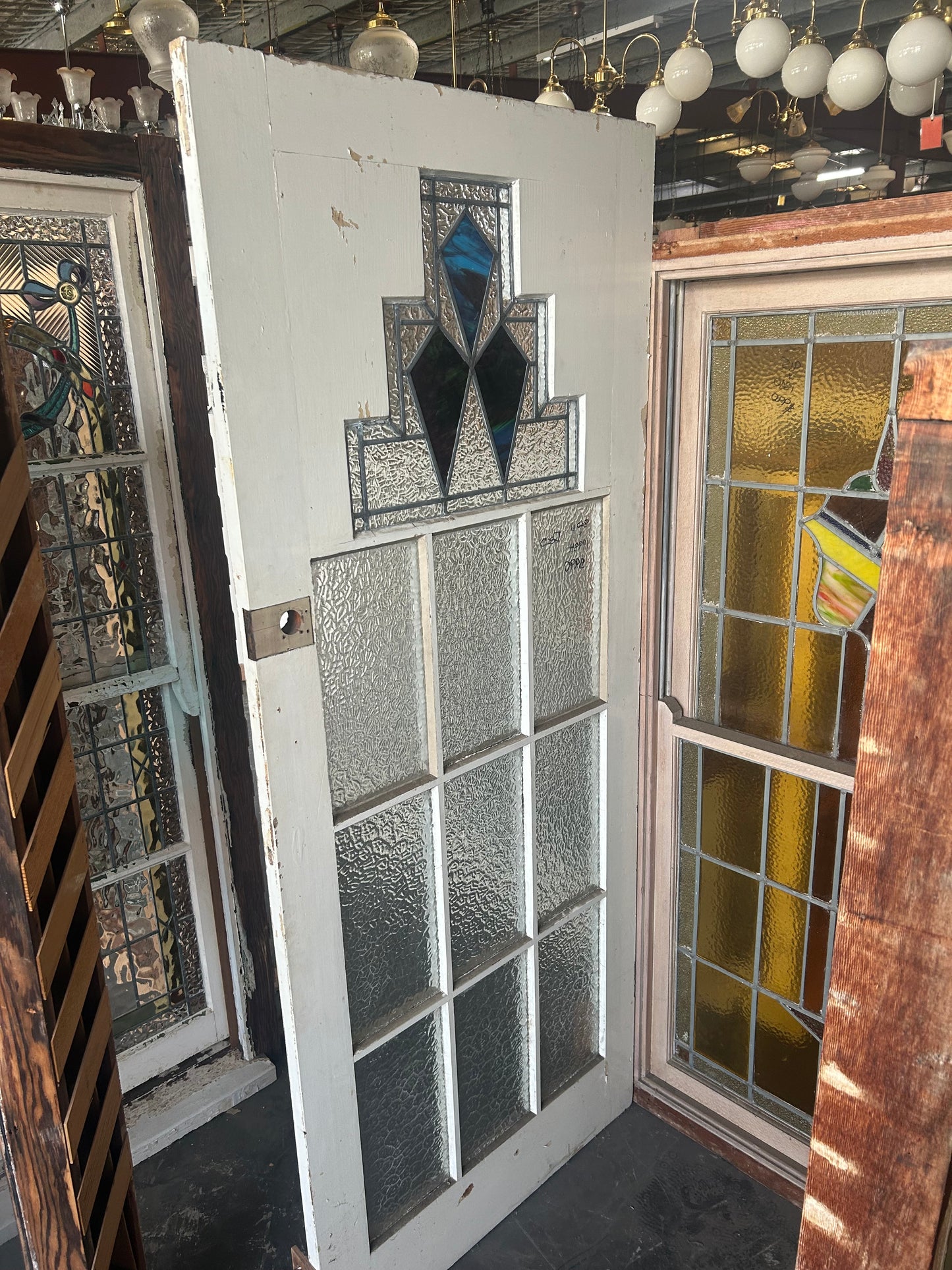 An original salvaged 1930s Art Deco style timber door painted white, featuring an upper window panel with geometric leadlight privacy glass and stained glass accents, on display at Chippendale Restorations.