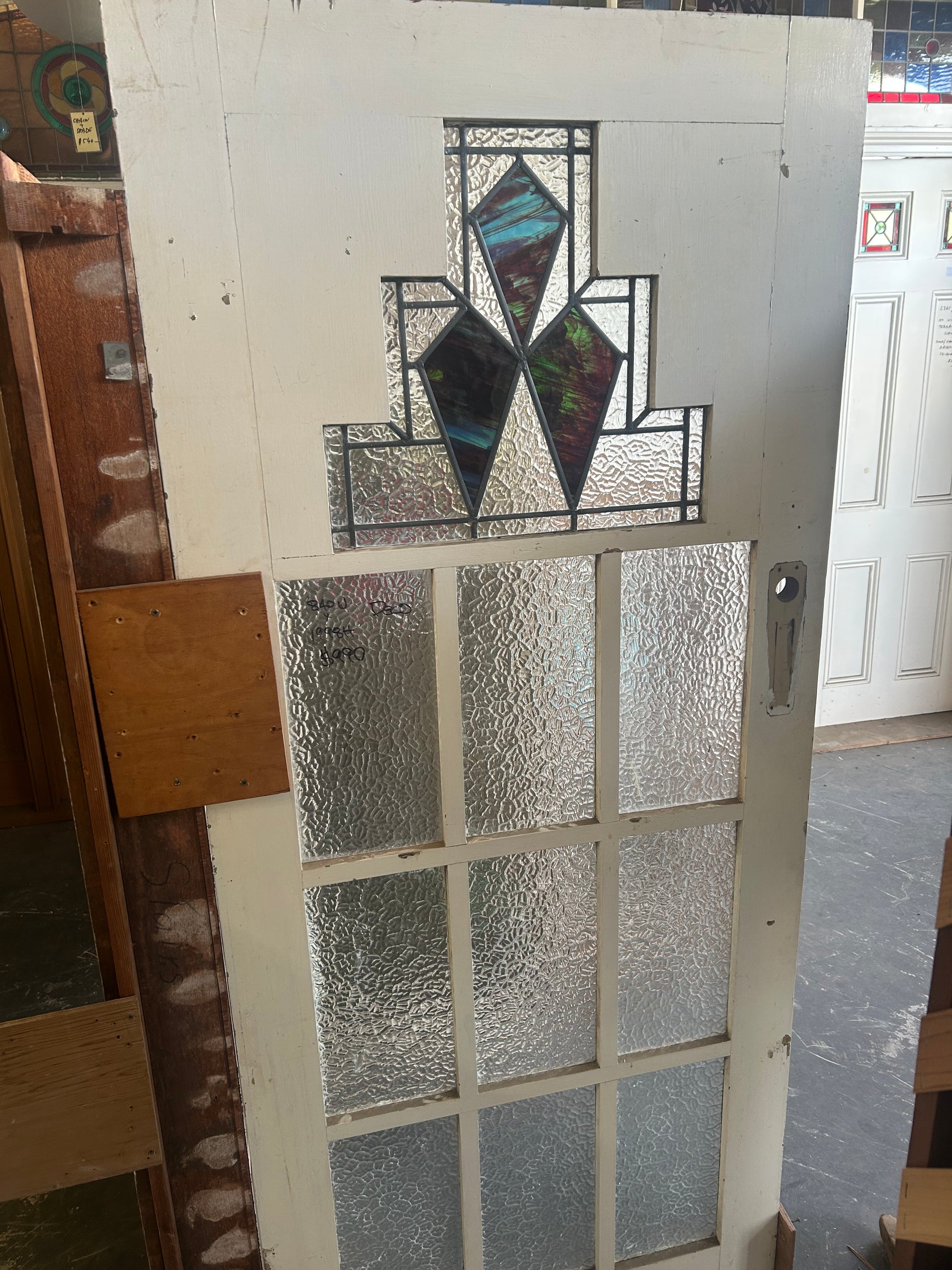 An original salvaged 1930s Art Deco style timber door painted white, featuring an upper window panel with geometric leadlight privacy glass and stained glass accents, on display at Chippendale Restorations.