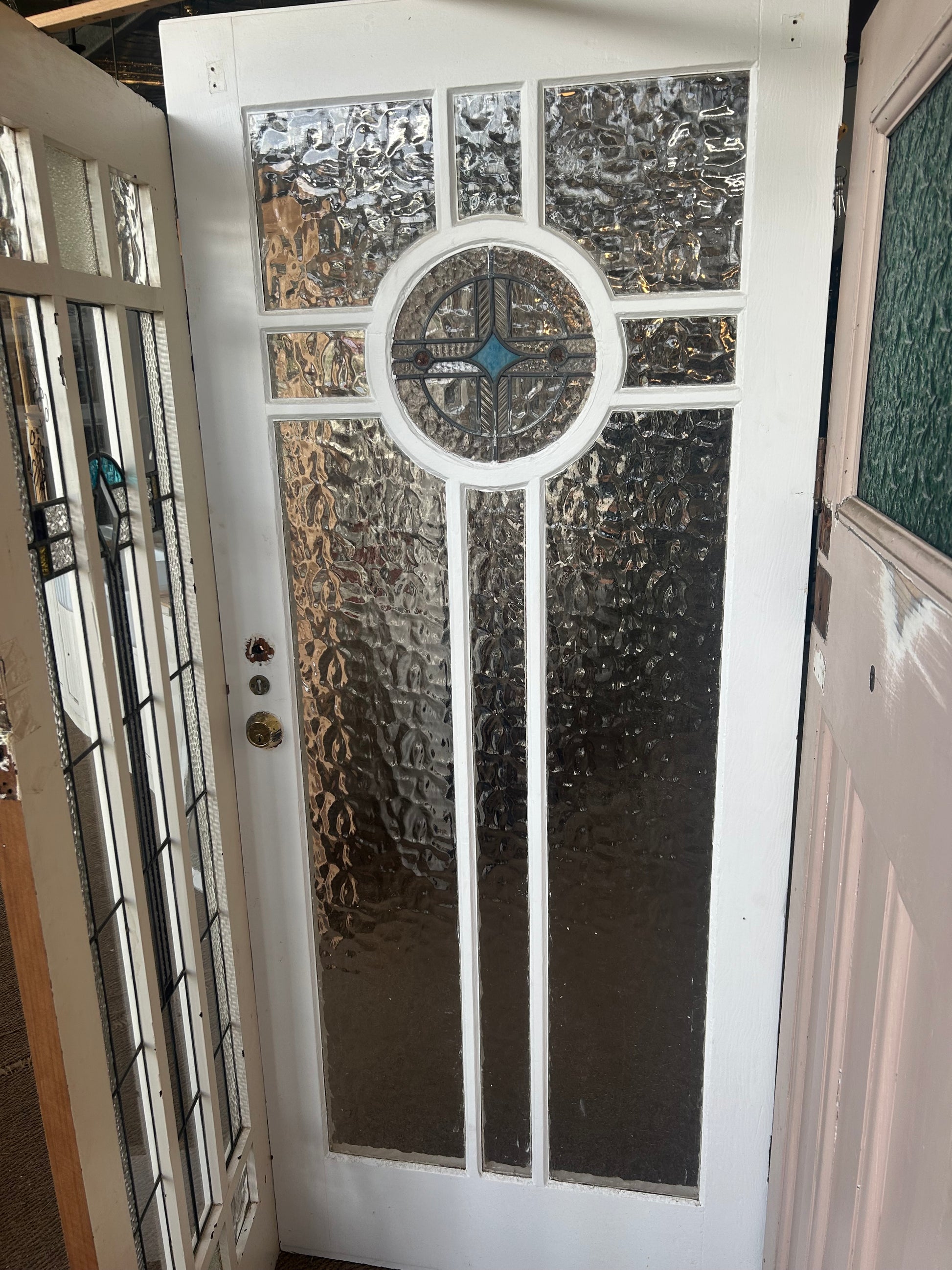 An original salvaged Federation style timber door painted white, featuring an upper window panel with textured privacy glass and a red and green leadlight floral design on display at Chippendale Restorations.