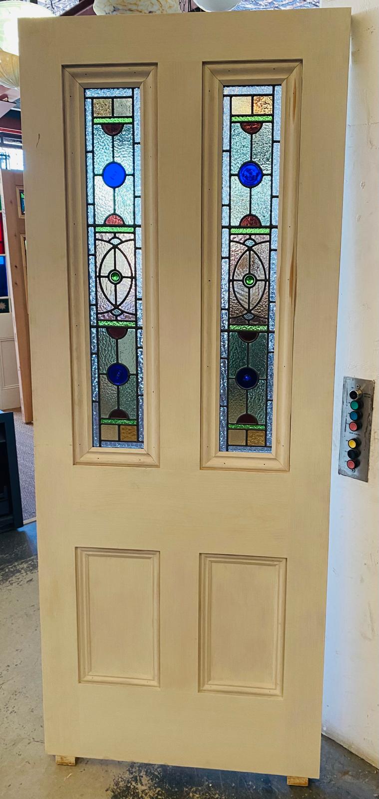 New Victorian four-panel door made of Western Red Cedar, featuring two vertical, rectangular leadlight glass panels. The leadlight design includes prominent round blue glass jewels, and green, amber, and red accents against a clear textured background.