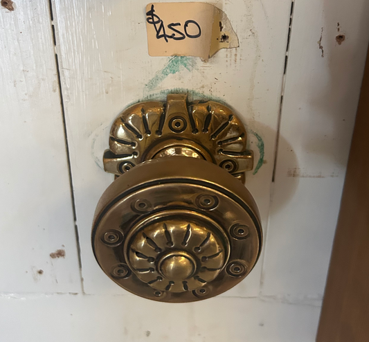 A close-up of an authentic, salvaged antique centre door knob made of solid brass with a deep, natural aged patina. The knob features a classic circular design with a stepped rose plate and visible wear that highlights its historical character and superior second-hand quality.