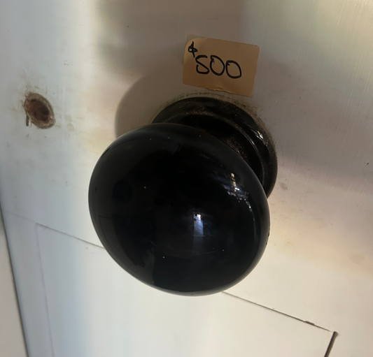 A close-up of an authentic, salvaged antique centre door knob made of solid brass with a deep, natural aged patina. The knob features a classic circular design with a stepped rose plate and visible wear that highlights its historical character and superior second-hand quality.