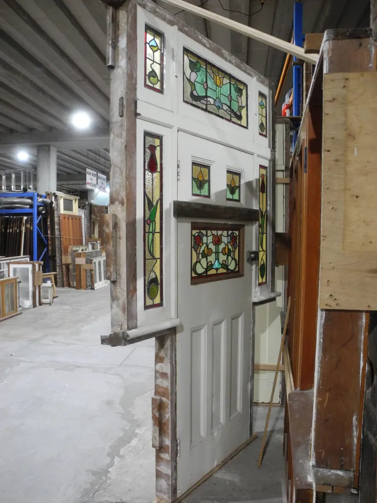 A spectacular original salvaged timber Federation entranceway door painted white, showcasing a large upper window with intricate textured privacy leadlight glass and vibrant red and amber stained glass accents on display at Chippendale Restorations.