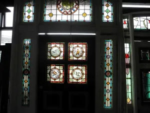 Close-up of an antique hand-painted glass roundel showing birds on branches inside a Victorian leadlight transom window frame.